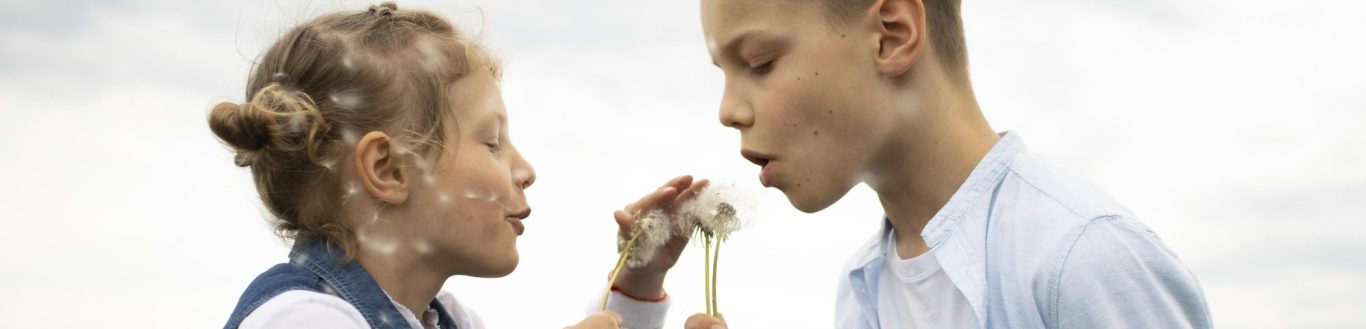 Pusteblume Ein Junge und ein Mädchen pusten Pusteblumen die sie in der Mitte zwischen sich halten.